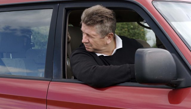 A man drives a car and looks backwards out the window