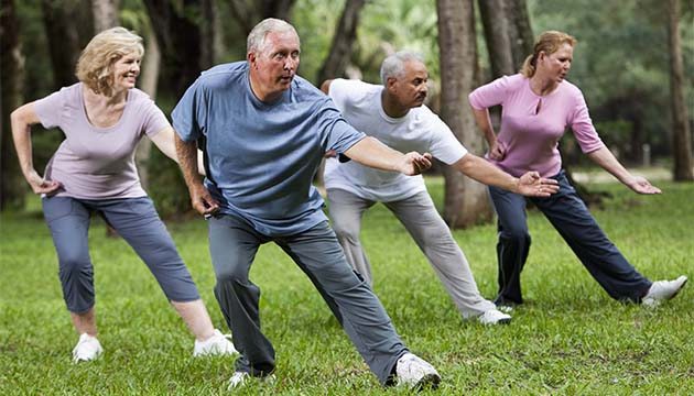 A group of older people doing tai chi for exercise in a forest or park setting