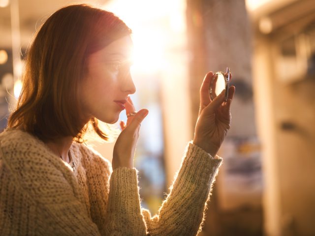A woman looks into a pocket mirror to adjust make-up