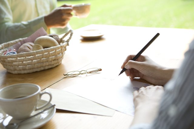 Close-up of hands writing a letter with glasses on the table