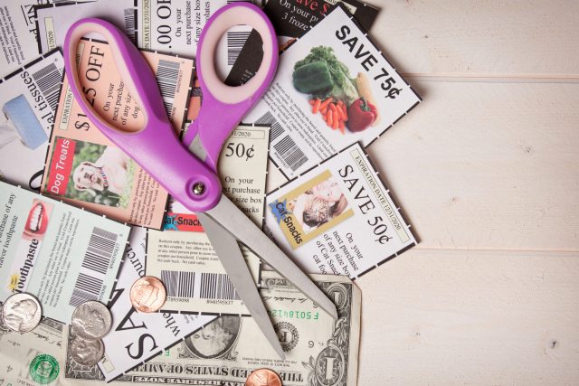 Purple handled scissors laying over clipped coupons