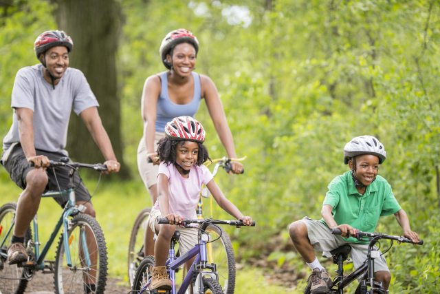 A family with helmets on, smile while enjoy a bicycle ride