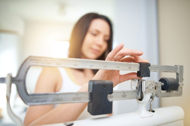 A woman adjusts a balance on a scale while weighing herself