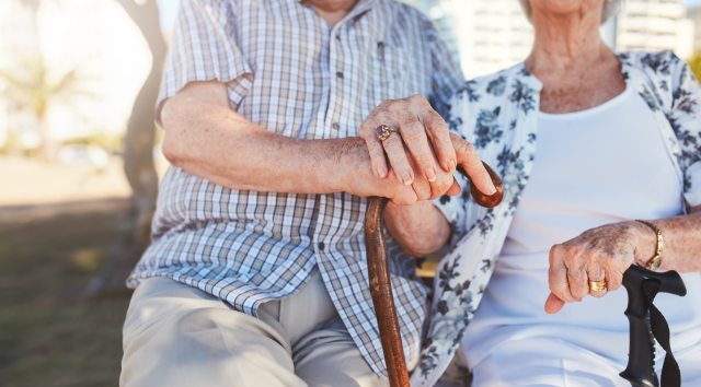 Elderly couple holding hands, a cane and other walking devices