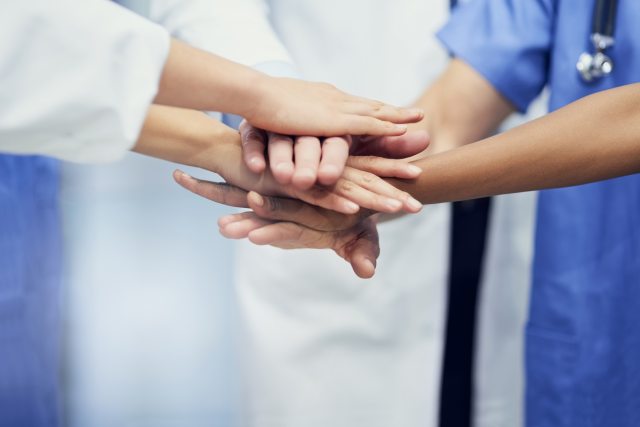 Health care providers in doctors jacket and scrubs stack hands