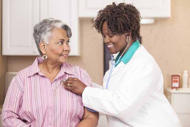 A healthcare provider smiles and checks a patient's heart rate