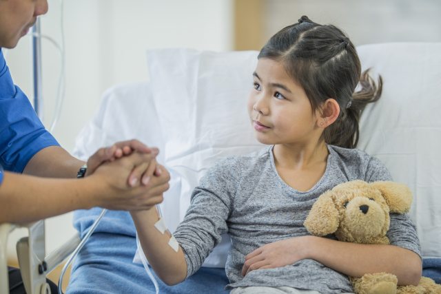 Young girl holding a teddy bear while resting in a patient bed