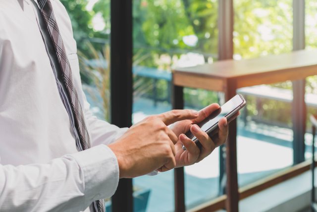 Man in a shirt and tie with a close-up of hand holding a mobile phone