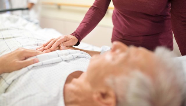 Woman comforting a male patient while he lays in a hospital bed