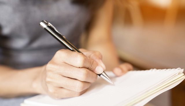 Close-up of hand and pen writing on paper