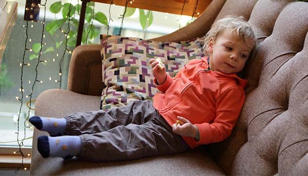A  young child sits on a couch eating a snack