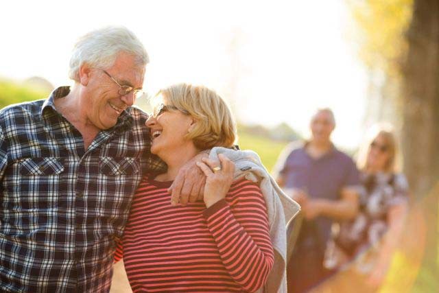 An older couple in the foreground smile and laugh with each other while another couple walks behind