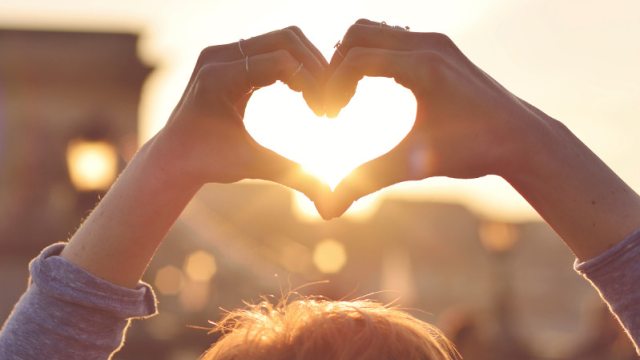 Close-up of hands in a heart shape with the sunlight beaming through