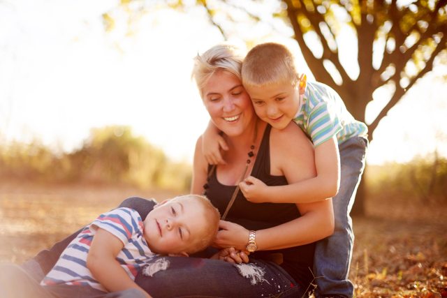 A mom and two young boys smiling and cuddling in a forest setting