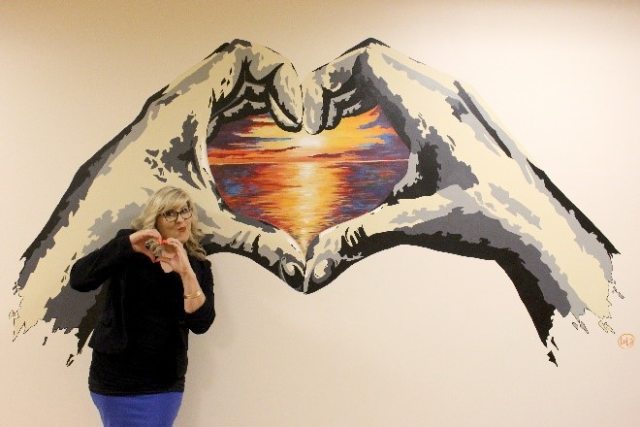 Lola Buckwald makes heart-hands next to her hand-themed mural