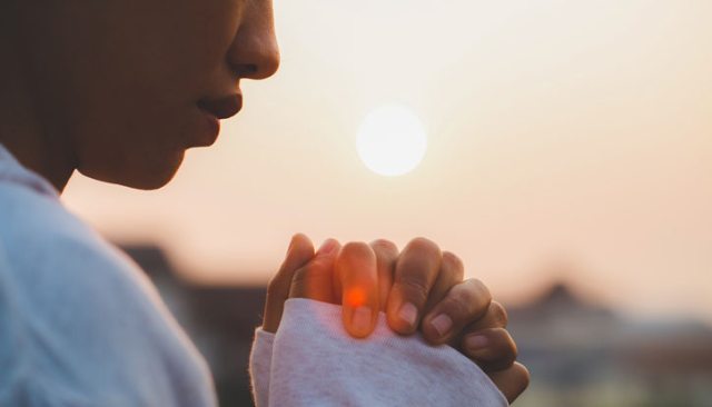 Close-up of a person with their hands folded with the setting sun in the background