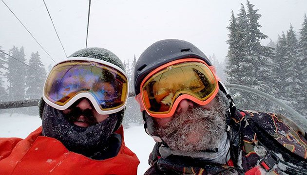 Skiers wearing ski masks and goggles ride the chair lift