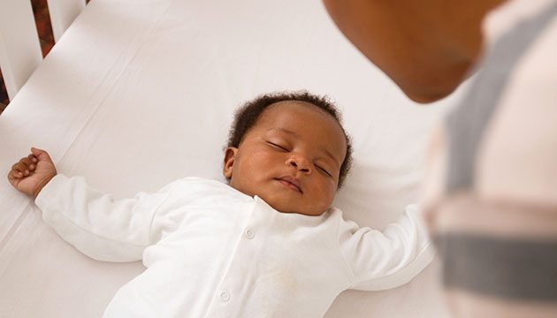 Small African American baby sleeps on its back in a crib