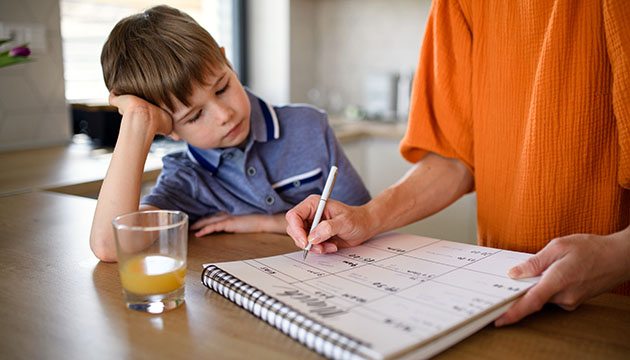 Young boy watches his mom write on a calendar